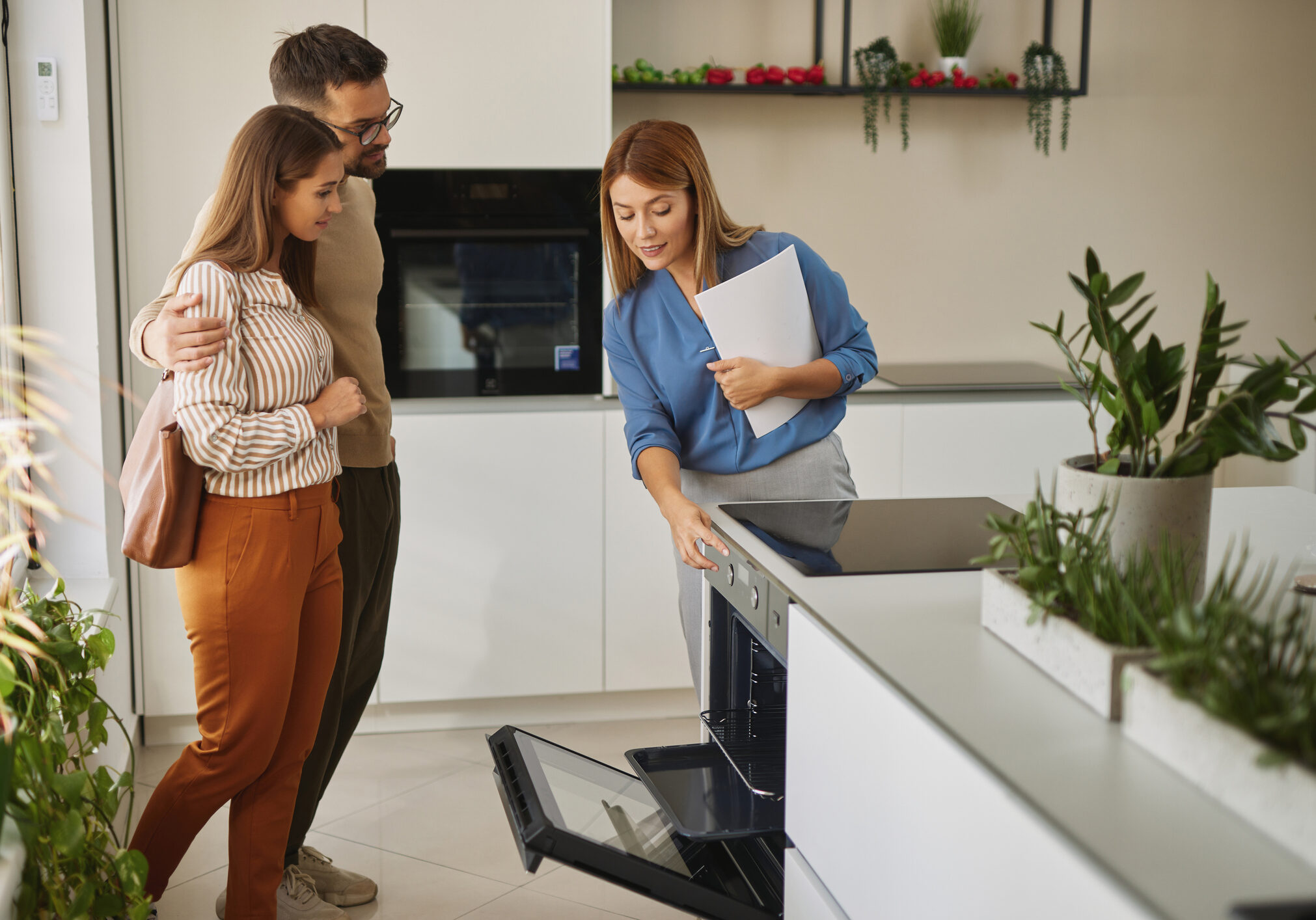 Female shop assistant helping young couple choose new electric stove